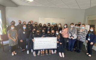 Mechanicville Girls Soccer Team holding a large check and smiling with masks over their faces.
